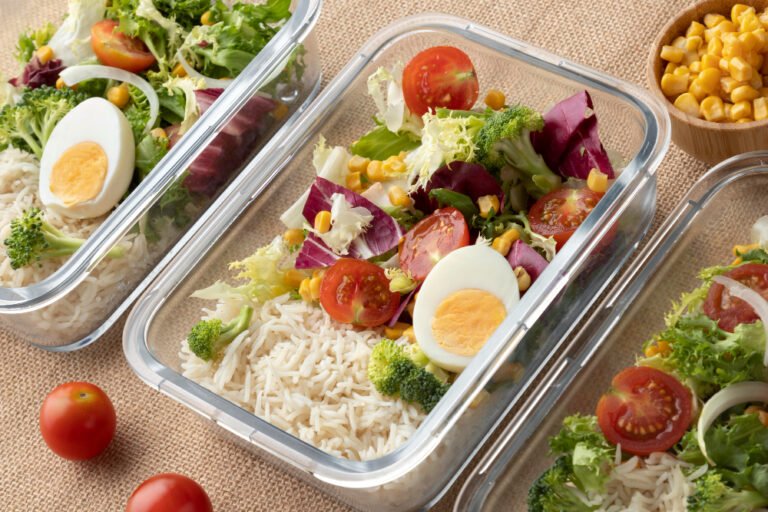 Glass meal prep containers with rice, boiled eggs, cherry tomatoes and mixed salad greens