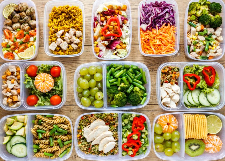 Overhead grid of meal prep containers with colorful ingredients including mushrooms, rice, broccoli and fruits